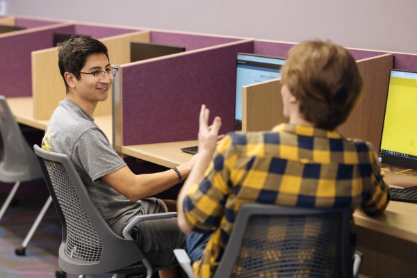 Two male students chat in front of computers in a lab