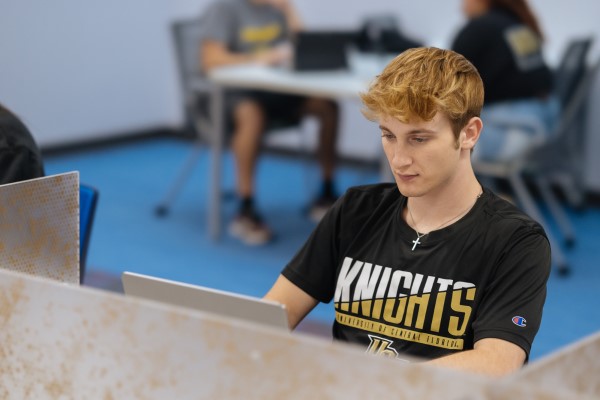 A male student sits at a desk with a laptop in front